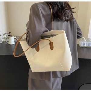 Side view of large cream tote bag with brown straps worn with a grey blazer