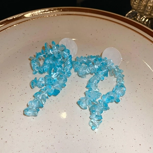 Detailed macro view of long tassel earrings with blue resin stones on a ceramic plate