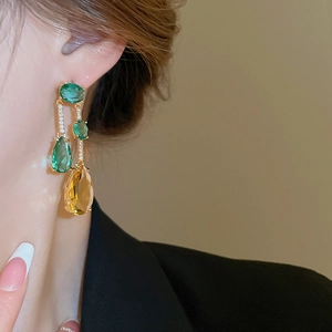 Gros plan de boucles d'oreilles dorées avec zircons vert émeraude et jaune ambre sur mannequin