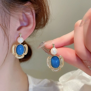Detail of vintage style earrings with white pearl and blue oval gemstone in gold finish