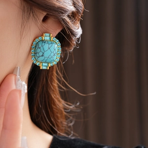 Close-up of vintage gold earrings with turquoise stone and blue rhinestones on model