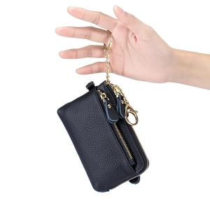 Minimalist black pebble leather coin purse with golden zipper and keychain held by hand