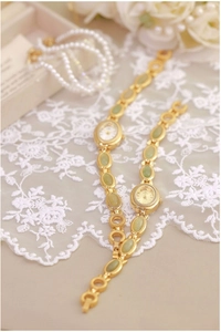 Detail view of vintage gold chain watch with green jade-like stones on white lace