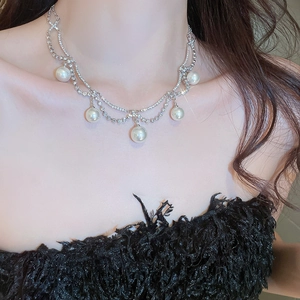 Detail shot of a double-layer pearl and rhinestone necklace on a black feather outfit
