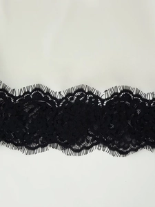 Makroaufnahme von eleganter schwarzer Wimpernspitze auf beigefarbenem Satinstoff-Detail