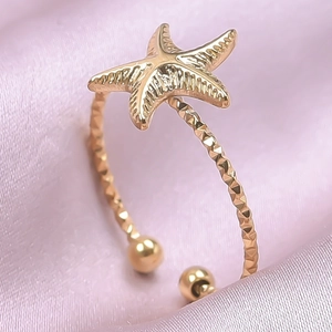 Makrodetail eines goldenen Seestern-Rings mit strukturierter Ringschiene auf Seide