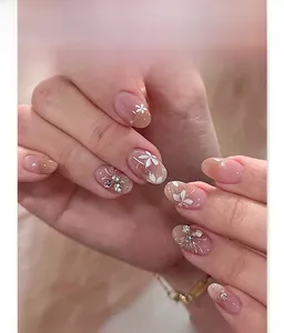 Close-up of pink blush press-on nails with white flower art and silver rhinestones