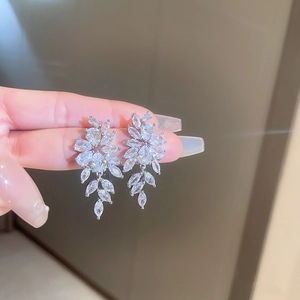Macro shot of silver leaf tassel earrings with sparkling zircon crystals on hand