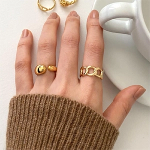Detail of gold water drop and chain link rings worn with cozy knitwear and coffee