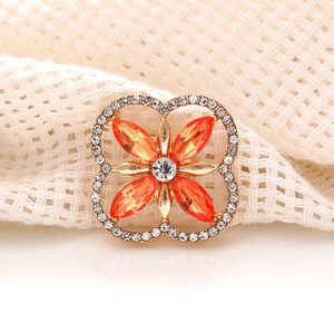 Detailed macro view of a gold four-leaf clover brooch with orange and clear crystals