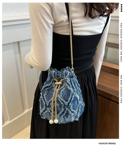 Detail of blue denim bucket bag with frayed diamond quilting, gold chain and pearl charms