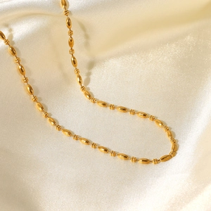 Dettaglio della collana a catena con perline placcata oro 18K su tessuto di seta beige