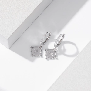 Macro shot of silver S925 earrings with diamond-set hoops and compass star charms