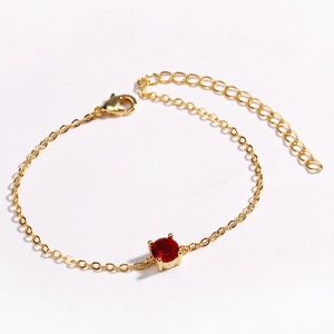 Detailed view of a gold bracelet featuring a red gemstone center and adjustable lobster clasp