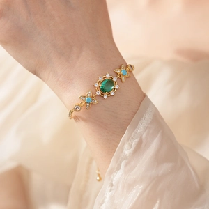 Bracelet doré vintage avec pierre ovale verte et fleurs en turquoise porté au poignet