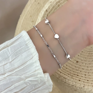 Detail of silver heart bracelets layering with a minimalist chain on a model wrist