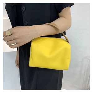Minimalist yellow PU leather handbag with khaki handle held by a model in black outfit