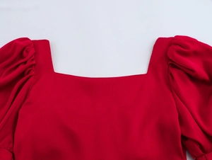 Detail van een rode jurk met vierkante halslijn en geplooide pofmouwen op wit canvas