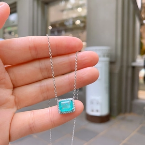 Close-up of a silver necklace featuring a square emerald zircon pendant held by hand