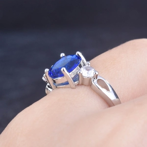 Three-stone open ring with large oval blue sapphire and clear side stones on model finger