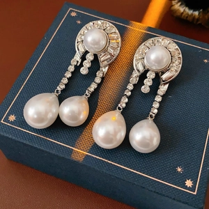 Dettaglio di orecchini pendenti in argento con perle bianche e strass su scatola blu