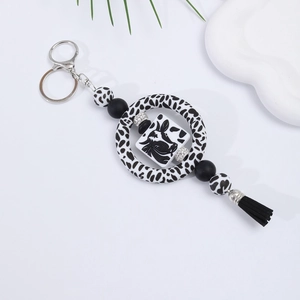 Silicone cow print keychain with beads and black tassel on a clean aesthetic background