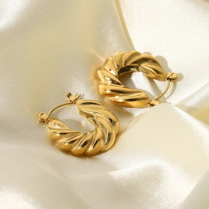 Macro view of gold plated twisted hoop earrings on beige silk satin background