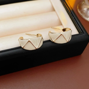 Macro shot of vintage C-shape gold earrings with white enamel patterns in a jewelry box