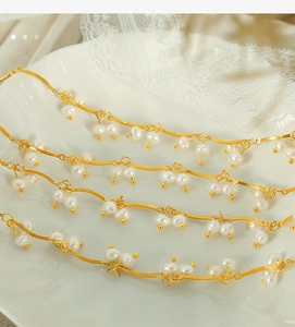 Close-up of golden wavy chain with freshwater pearl tassels on white lace background