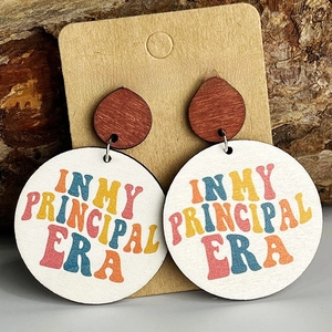 Close-up of wood earrings with In My Principal Era text on a natural bark background
