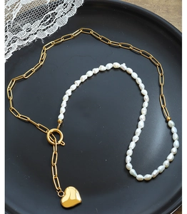 Close-up of baroque pearl necklace with gold heart pendant and toggle clasp on black tray