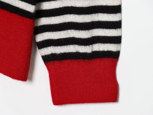 Détail d'un pull en maille avec rayures noires et blanches et poignet côtelé rouge