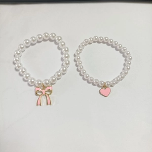 Detail of beaded bracelets with pink bow and heart pendants on white background