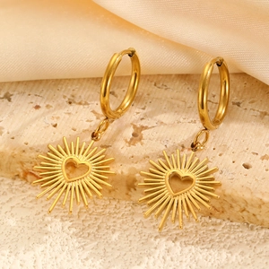 Détails de créoles dorées avec pendentifs cœur soleil sur fond en satin de couleur crème