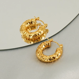 Detail of gold U-shaped hoop earrings with hammered metal texture on reflective surface