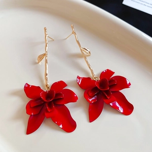 Detailed close-up of red floral earrings with golden leaf accents on a ceramic tray