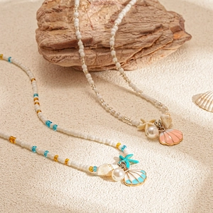 Handmade beaded necklaces with colorful shells, starfish and pearls on a beach sand background