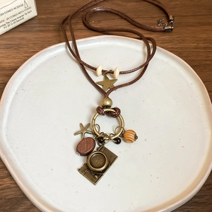 Macro detail of wax rope necklace with vintage brass camera and wooden bead pendants