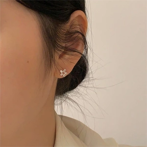 Close-up of a minimalist silver five-petal flower stud earring on a model ear