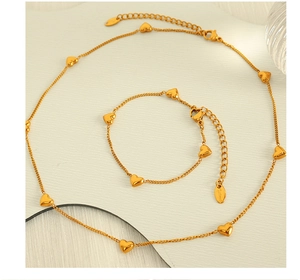 Close-up of golden stainless steel heart necklace and bracelet set on a textured surface