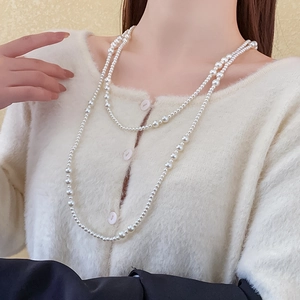 Detailed view of long double-layer pearl necklace on a beige knit cardigan for a chic look