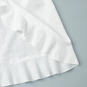 Detailed macro view showing the white linen fabric texture and elegant ruffle seam details