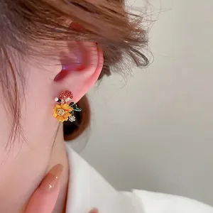 Elegant yellow flower stud earrings with green leaf accent on female model profile