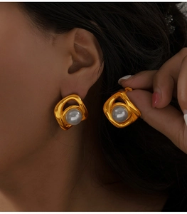 Détail de la boucle d'oreille géométrique dorée avec perle blanche sur modèle