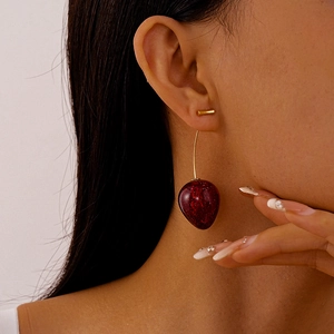 Close-up of deep red cherry acrylic earrings with golden metal stems worn on a model