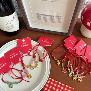 Handmade red braided cord bracelet with gold charms and glass beads on a vintage tray