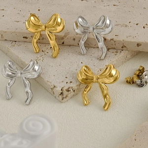 Bow-shaped 18k gold and silver stainless steel earrings displayed on white stone