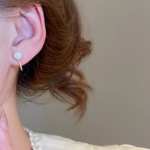Close-up of a white pearl ear clip on a model's ear with elegant gold metal setting