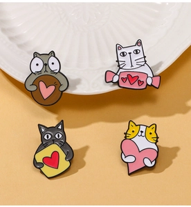 Detail of four cute cartoon cat enamel pins with heart patterns on a ceramic plate