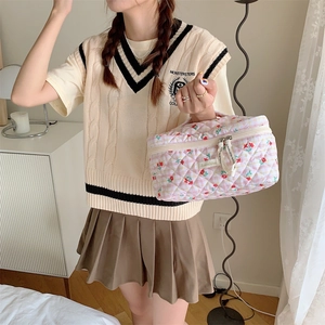 Pink floral quilted cosmetic bag with top handle shown in a lifestyle college style setting